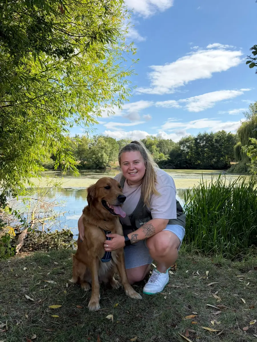 Aimee crouching beside Oakley at the edge of a lake